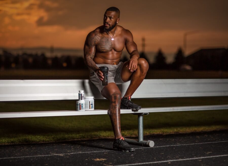 best sports supplements for recovery after football – Muscular athlete sitting on a bench with supplements, enjoying a sunset at an outdoor stadium.