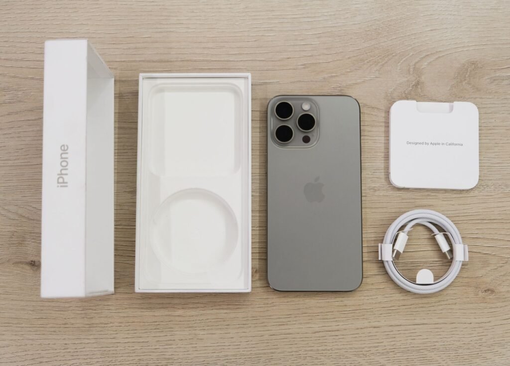 buy original iPhone accessories from Amazon in Pakistan – Flat lay view of the newest Apple iPhone model, box, and charging accessories on a wooden table.