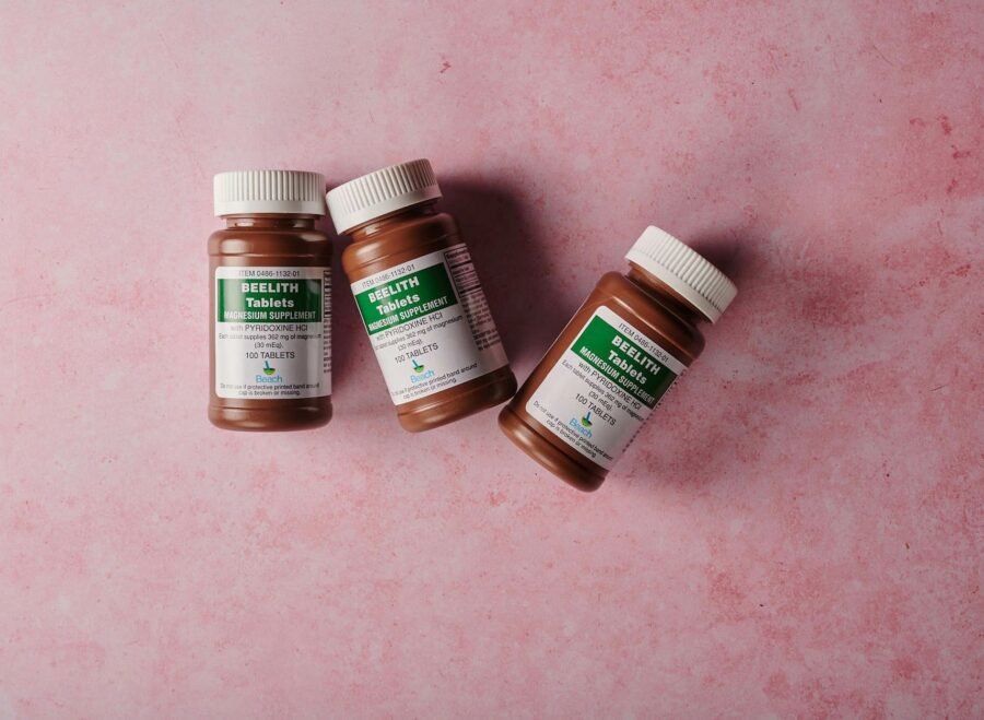 fake health supplements Pakistan – Three brown bottles of magnesium tablets on a soft pink background, ideal for health-themed content.