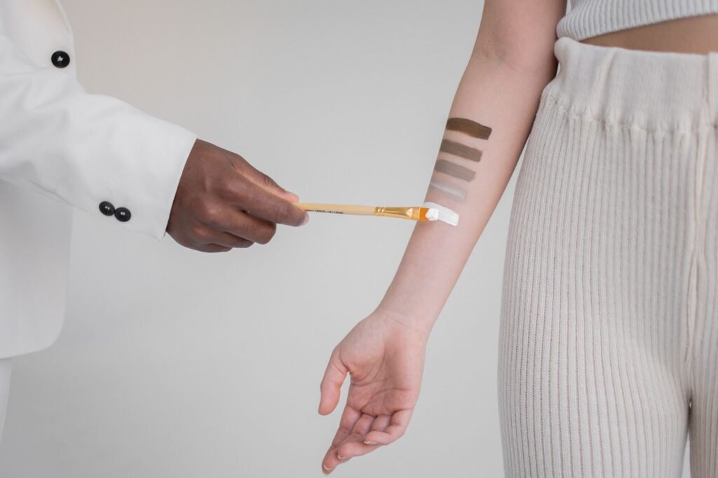 FENTY BEAUTY Pakistan proxy shopping – Crop anonymous African American male with brush applying paint in different colors of skin tone on female hand against gray background