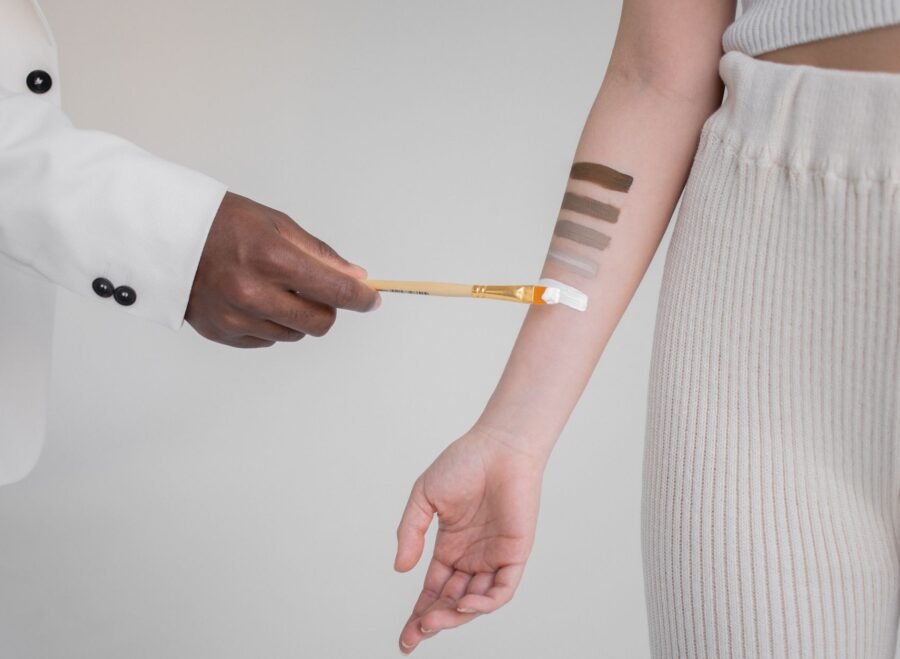 FENTY BEAUTY Pakistan proxy shopping – Crop anonymous African American male with brush applying paint in different colors of skin tone on female hand against gray background
