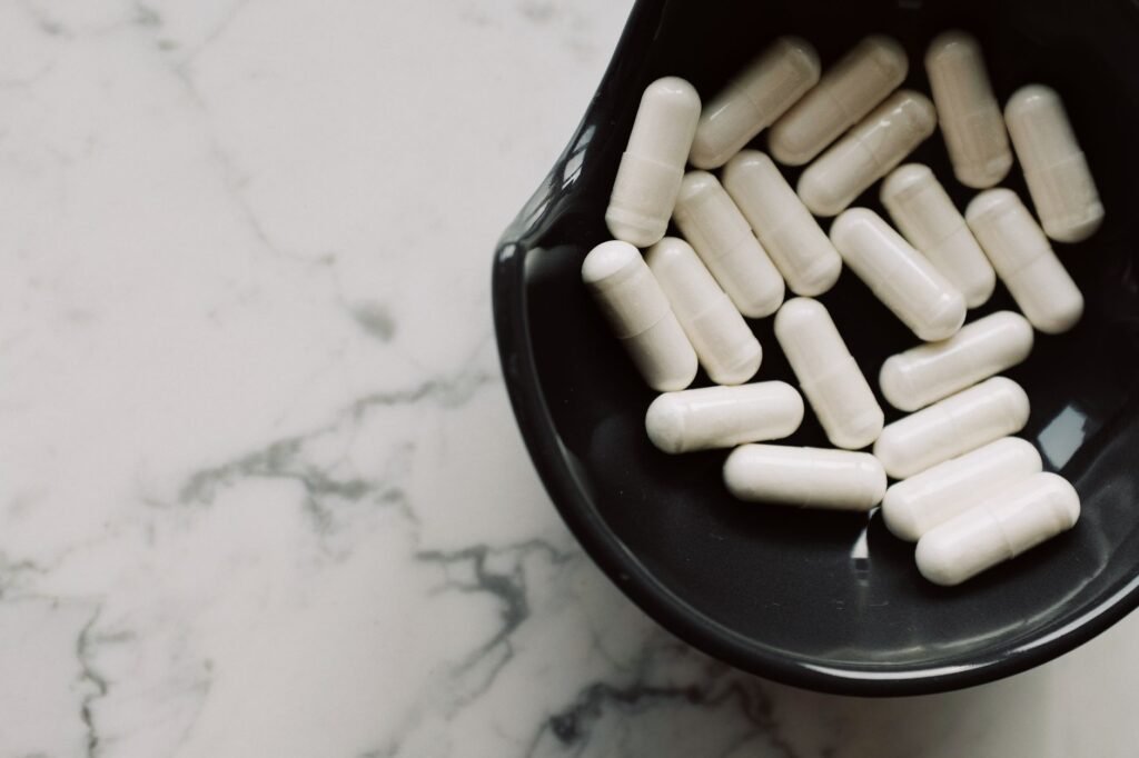 magnesium supplements for stress Pakistan – Close-up of white capsules in a black bowl on a marble surface, symbolizing healthcare and medication.