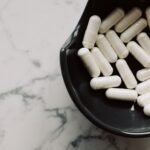 magnesium supplements for stress Pakistan – Close-up of white capsules in a black bowl on a marble surface, symbolizing healthcare and medication.