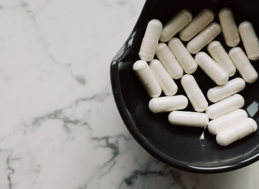 magnesium supplements for stress Pakistan – Close-up of white capsules in a black bowl on a marble surface, symbolizing healthcare and medication.