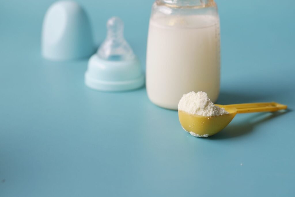 US baby formula in Pakistan – Close-up of baby milk formula powder in a yellow scoop with a bottle on a blue background.