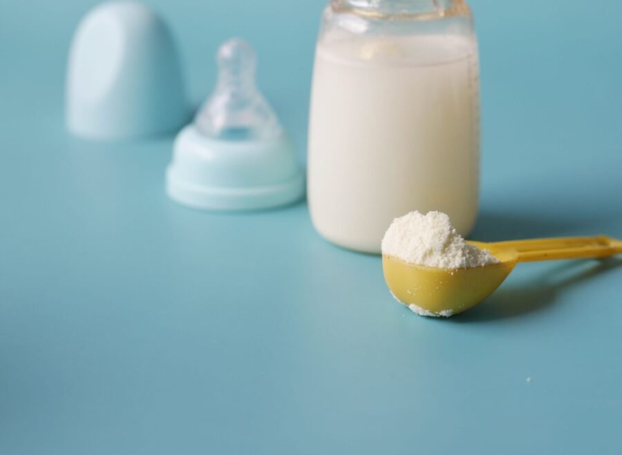 US baby formula in Pakistan – Close-up of baby milk formula powder in a yellow scoop with a bottle on a blue background.