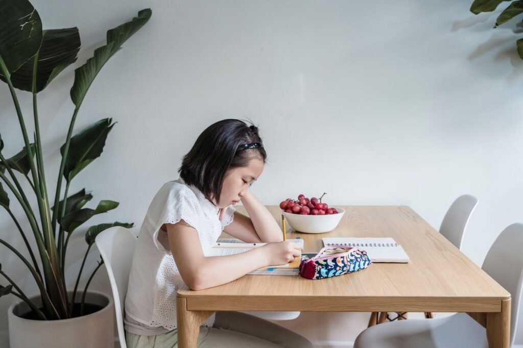 baby study table chair set price in pakistan – Asian child reading and writing at home, surrounded by plants and books, creating a learning environment.