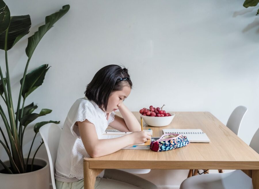 baby study table chair set price in pakistan – Asian child reading and writing at home, surrounded by plants and books, creating a learning environment.