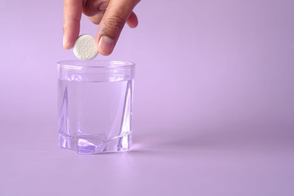 hydration supplements for summer Pakistan – Close-up of a tablet being dropped into a glass of water on a purple background, creating bubbles.