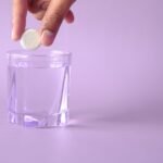 hydration supplements for summer Pakistan – Close-up of a tablet being dropped into a glass of water on a purple background, creating bubbles.