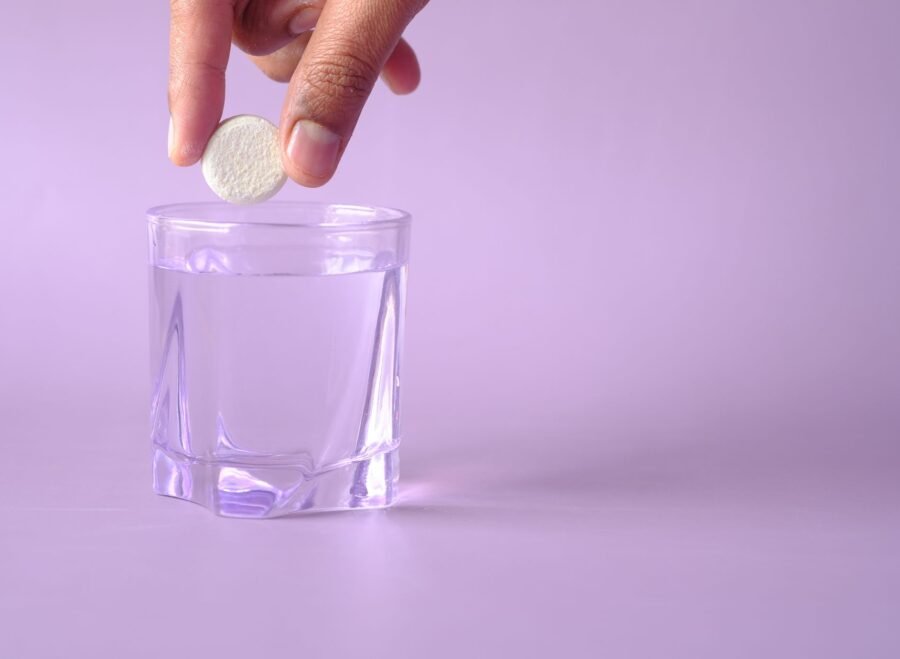 hydration supplements for summer Pakistan – Close-up of a tablet being dropped into a glass of water on a purple background, creating bubbles.