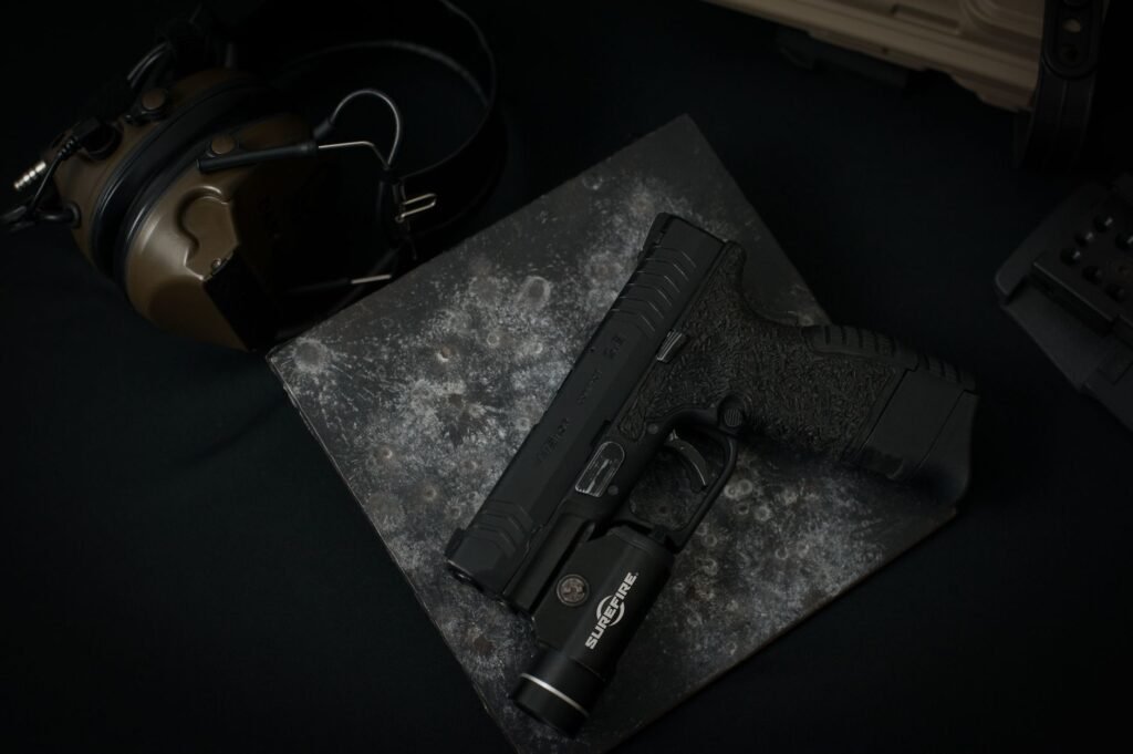 search light price in pakistan – Detailed view of a black handgun with attached tactical flashlight on dark textured surface.
