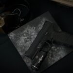 search light price in pakistan – Detailed view of a black handgun with attached tactical flashlight on dark textured surface.