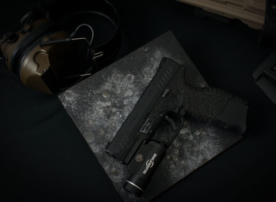 search light price in pakistan – Detailed view of a black handgun with attached tactical flashlight on dark textured surface.
