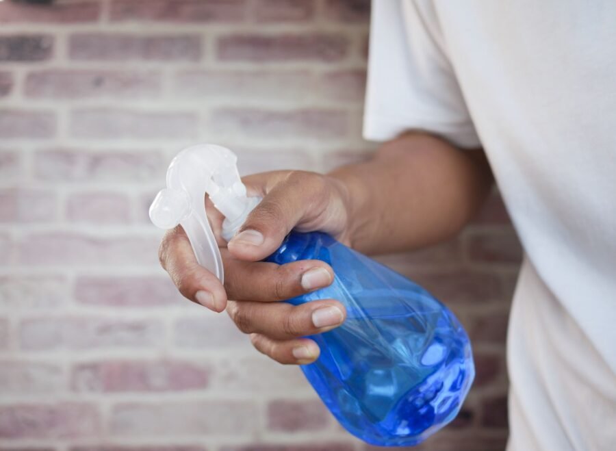stud spray price in pakistan – A close-up shot of a hand holding a blue spray bottle against a brick wall background.