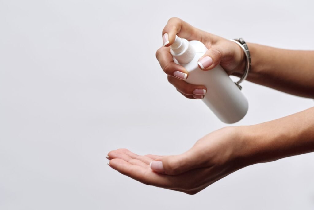 stud spray price in pakistan – Close-up of hands applying sanitizer from a white spray bottle, showing hygiene care.