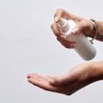 stud spray price in pakistan – Close-up of hands applying sanitizer from a white spray bottle, showing hygiene care.