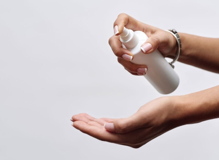 stud spray price in pakistan – Close-up of hands applying sanitizer from a white spray bottle, showing hygiene care.