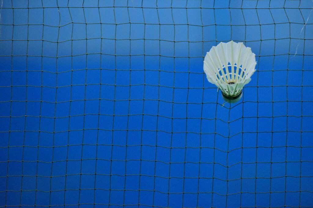 badminton net price in pakistan – Shuttlecock caught in badminton net on blue court, symbolizing sport and challenge.