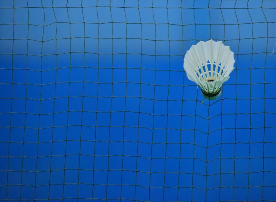 badminton net price in pakistan – Shuttlecock caught in badminton net on blue court, symbolizing sport and challenge.
