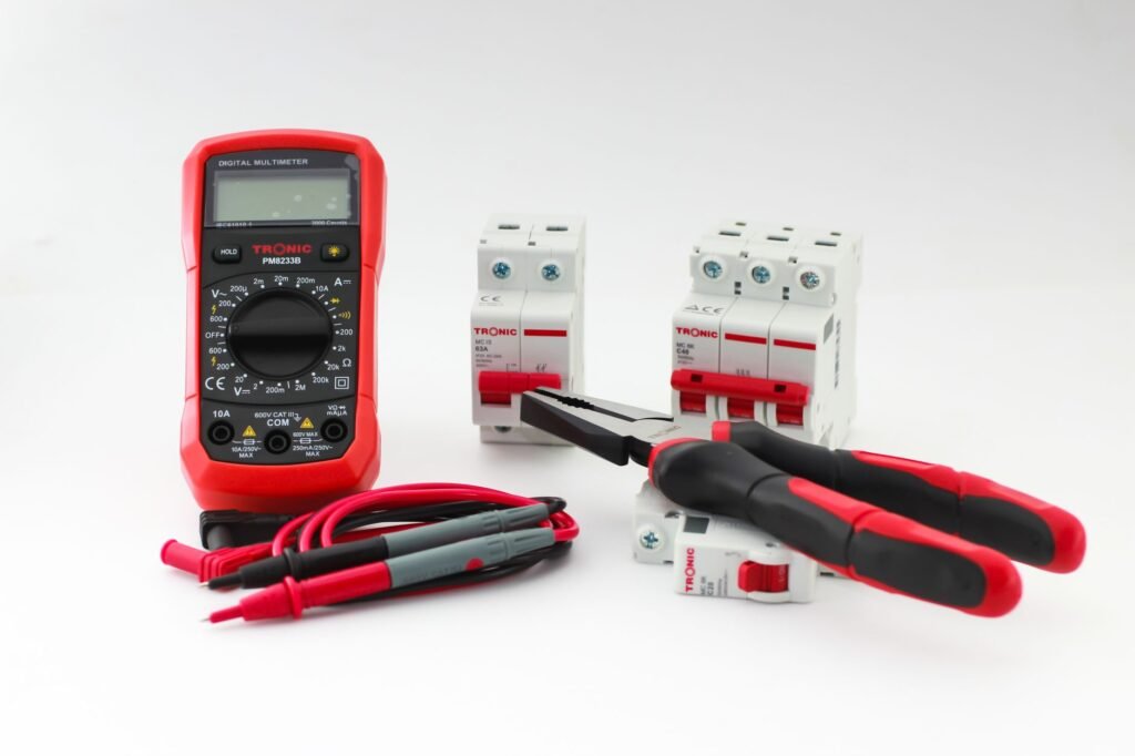 digital ampere meter – Close-up of a digital multimeter with electrical tools and circuit breakers on a white background.