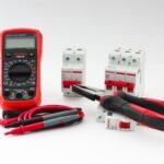 digital ampere meter – Close-up of a digital multimeter with electrical tools and circuit breakers on a white background.