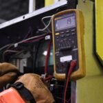 digital ampere meter – Electrician using a multimeter to fix industrial control panel wiring.