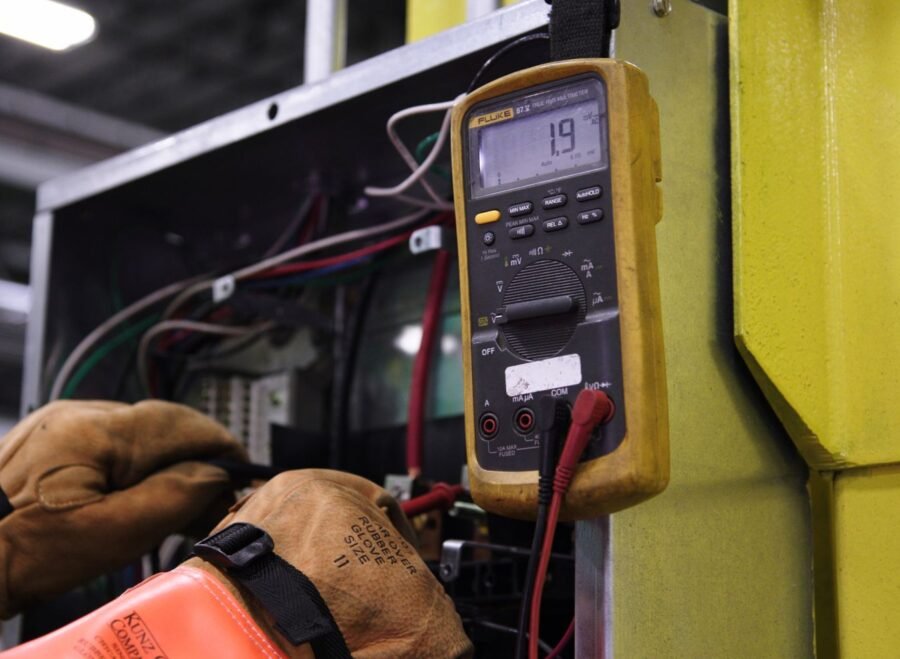 digital ampere meter – Electrician using a multimeter to fix industrial control panel wiring.