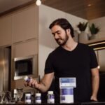 GNC Mega Men price in Pakistan – Man in a modern kitchen holding a vitamin supplement bottle, surrounded by health products.