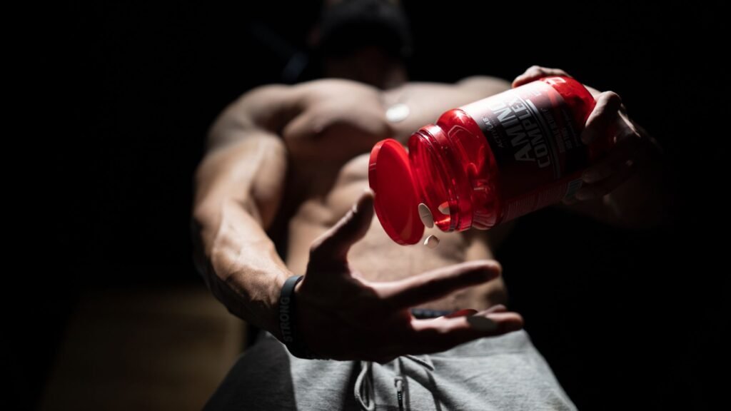 gnc mega men price in pakistan – Shirtless muscular man pouring protein supplements from a bottle, showcasing fitness and strength.