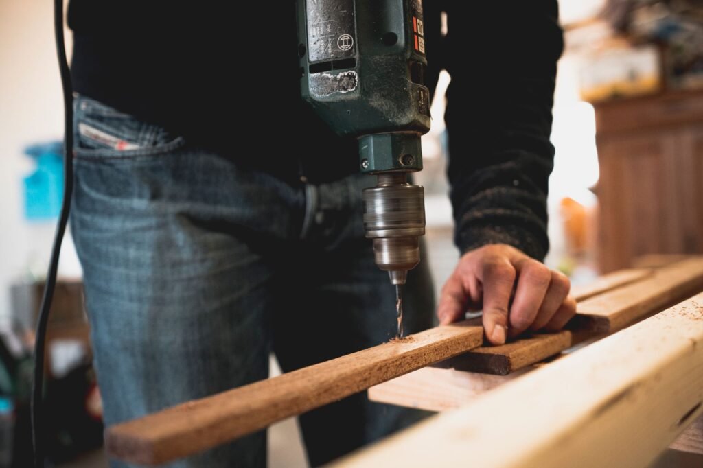 makita drill machine price in pakistan – Close-up of a person using an electric drill on a wooden plank, showcasing detailed woodworking skills.