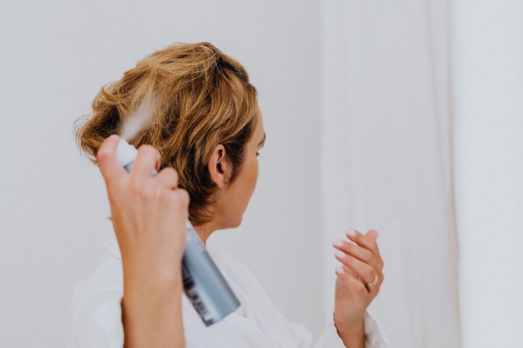 procomil delay spray in pakistan – A woman uses hair spray for styling in a bright indoor setting.