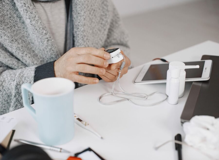 vein viewer price in pakistan – Close-up of hands using a health device at a desk with electronic gadgets and a cup.