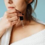 acnes c10 serum price in pakistan – Close-up of a woman in a bathrobe applying serum for skincare routine.