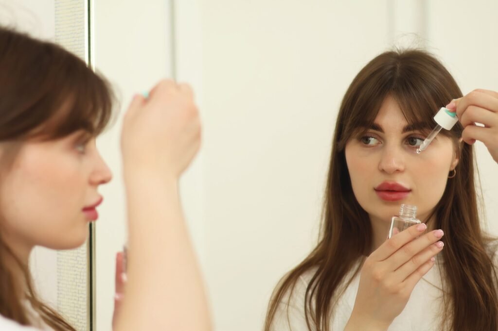acnes c10 serum price in pakistan – A young woman applying skincare serum in front of a mirror indoors. Perfect for beauty and self-care themes.