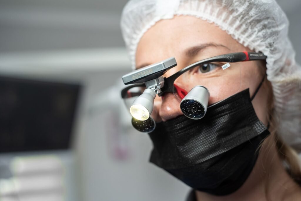 dental loupes price in pakistan – Female dentist wearing dental loupes and face mask, focused on patient care.
