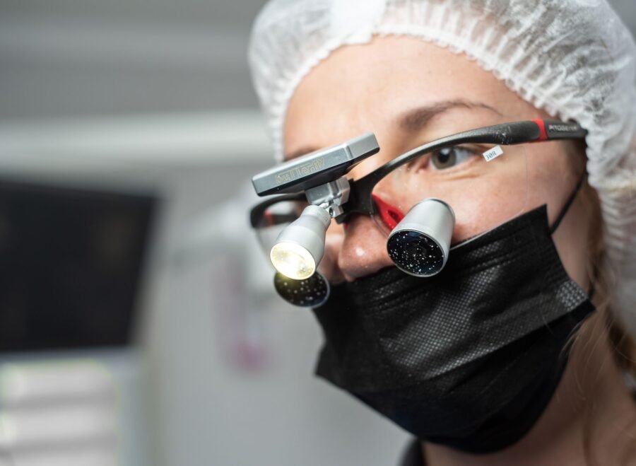 dental loupes price in pakistan – Female dentist wearing dental loupes and face mask, focused on patient care.