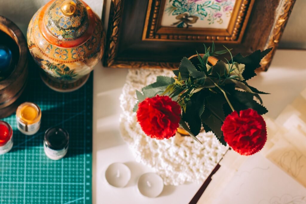 embroidery frame price in pakistan – Creative workspace with red carnations, framed art, and ornamental decor.