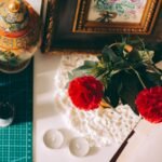 embroidery frame price in pakistan – Creative workspace with red carnations, framed art, and ornamental decor.