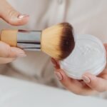 Etude face powder price in Pakistan – Close-up view of a hand applying face powder with a makeup brush, perfect for beauty and lifestyle concepts.