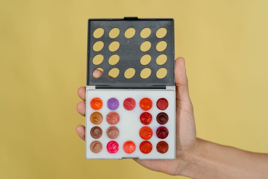 lip palette in pakistan – Hand holding a vibrant makeup palette with lipstick shades against a yellow backdrop.