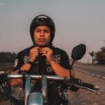 open face helmet pakistan – Man wearing a helmet adjusting it on his motorcycle during the day on an open road.