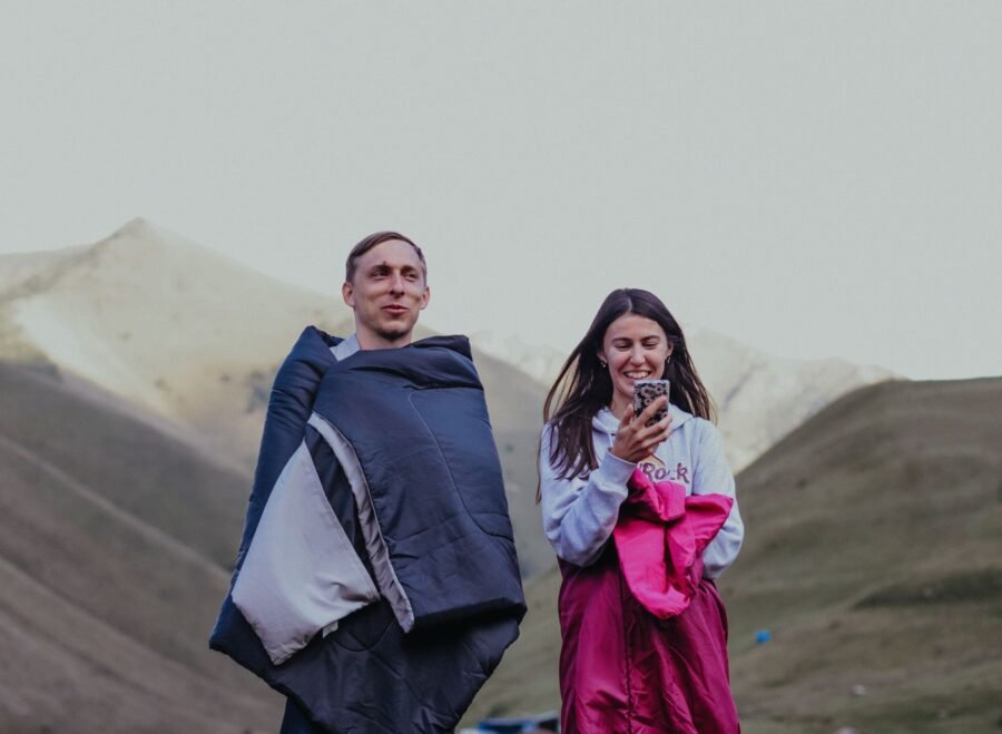 sleeping bag pakistan – A man and woman wrapped in sleeping bags enjoying nature and outdoor camping in mountainous terrain.